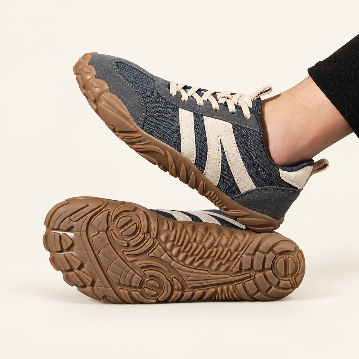 Carrera Urban™, zapatilla gris oscuro puesta y detalle de la suela sobre fondo crema.